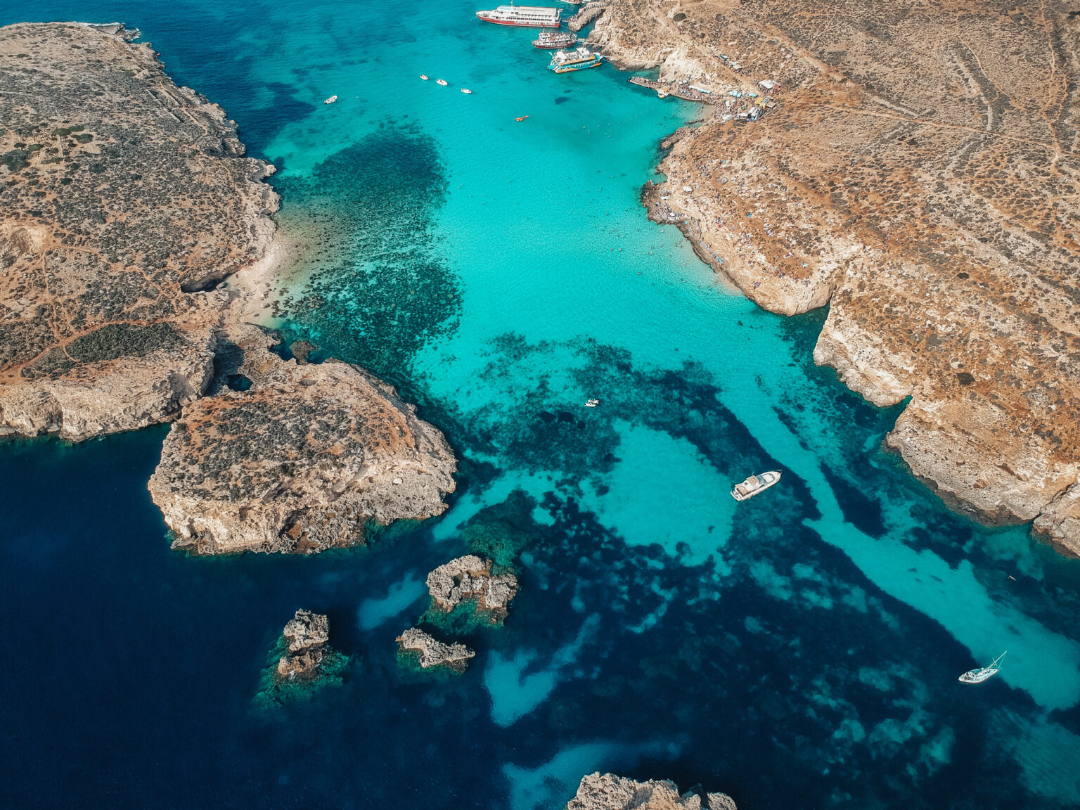 Stunning drone shot of Comino, Malta showcasing crystal-clear turquoise waters and rugged coastline, perfect for a Comino day trip adventure.
