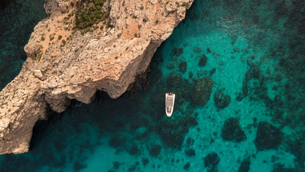 Aerial view of Crystal Lagoon in Malta with turquoise water, rocky cliffs, and boats exploring the bay—illustrating the experience of Boat Tours vs Jet Ski Tours in this popular Mediterranean destination.