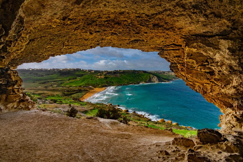 Scenic view from Calypso Cave overlooking Ramla Bay, showcasing golden sands, turquoise waters, and lush green hills in Gozo, Malta.