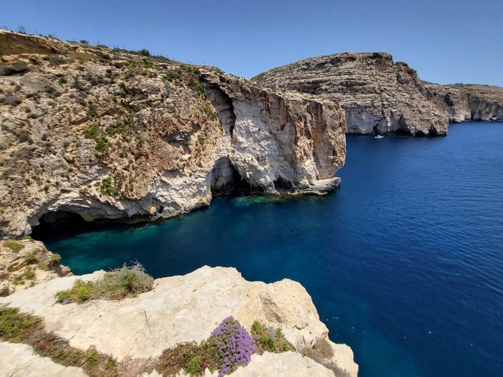 Crystal-clear turquoise waters of Blue Grotto, Malta, with dramatic limestone cliffs and sea caves in the background.