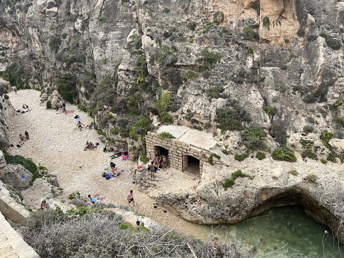 Tourists relaxing on the rocky shore in Wied-il-Ghasri, enjoying the tranquil atmosphere.