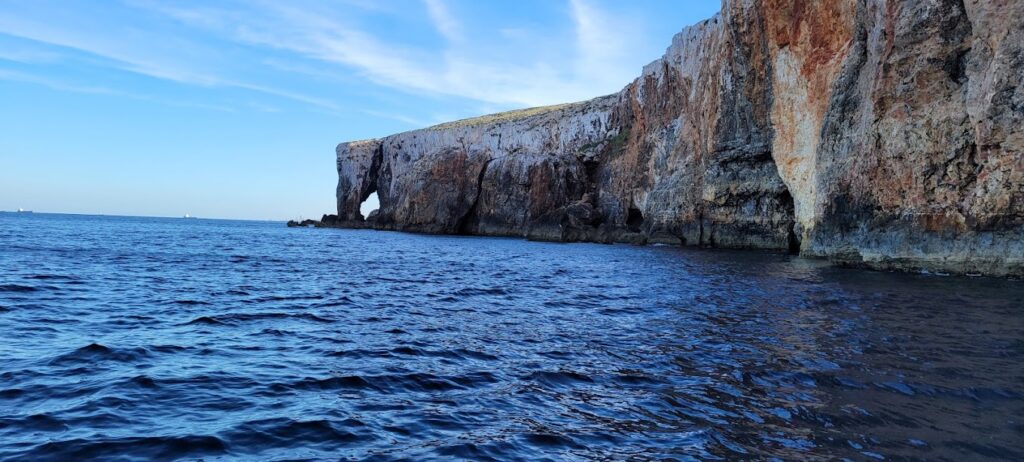 Scenic view of Elephant Rock, Malta, with unique rock formations resembling an elephant's head and tusks, set against a clear blue sky and calm turquoise waters.