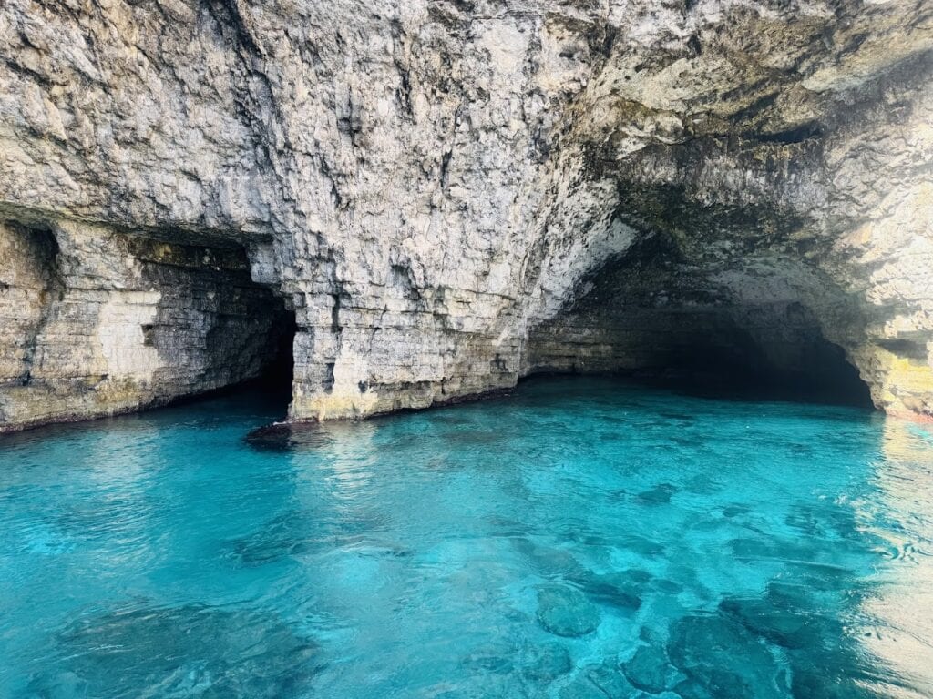 Scenic view of Santa Marija Caves on Comino Island, Malta, showcasing crystal-clear turquoise waters, rugged limestone cliffs, and hidden sea caves, popular for snorkeling and boat tours.