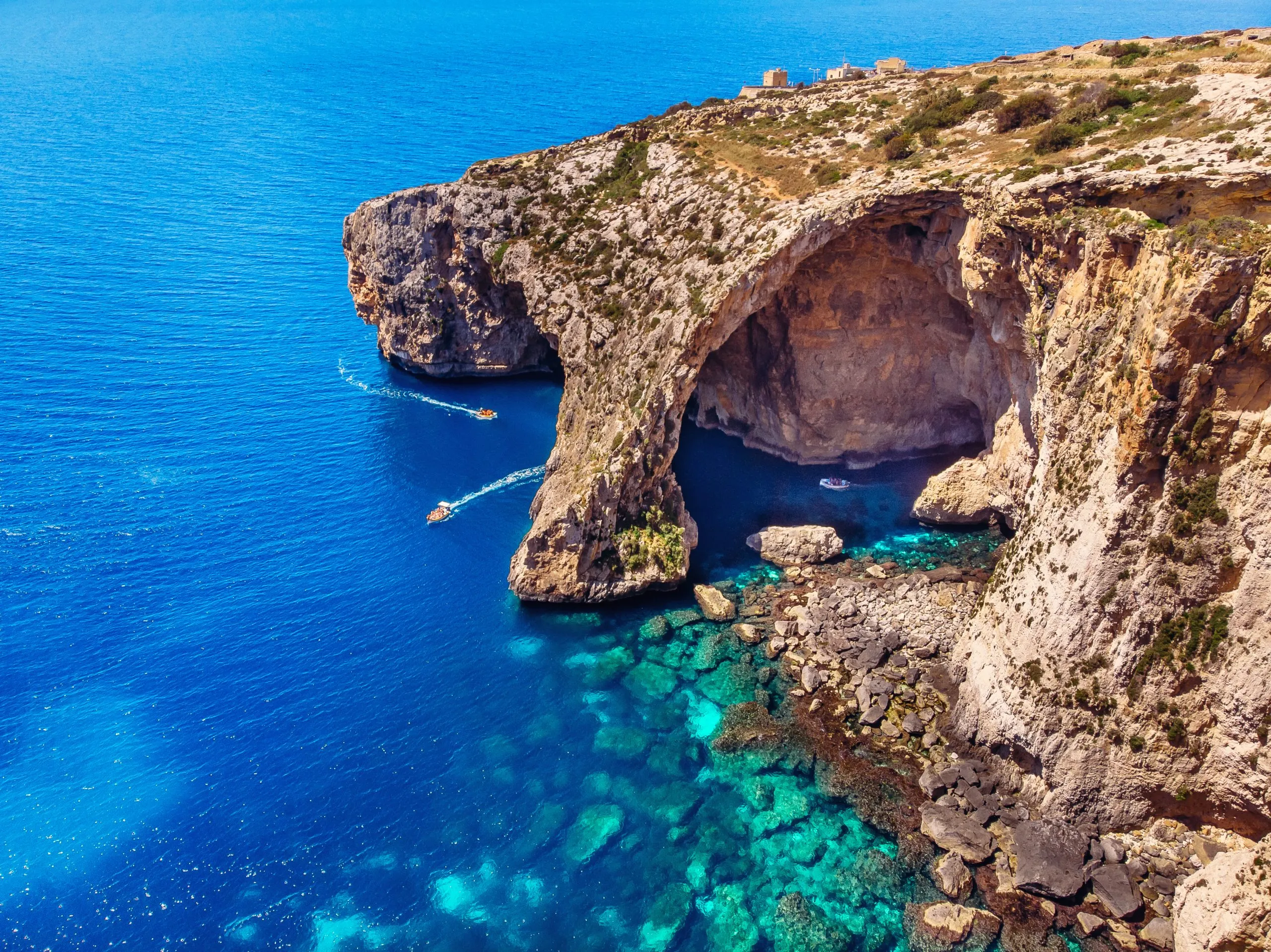 Scenic view of Blue Grotto, Malta, featuring stunning limestone sea caves and crystal-clear turquoise waters under a bright blue sky.