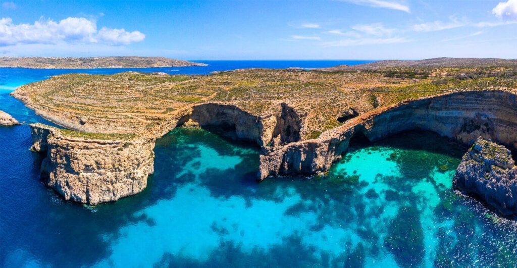 Crystal Lagoon, Malta – A breathtaking view of turquoise waters surrounded by dramatic limestone cliffs, offering a secluded and tranquil swimming spot near Comino.