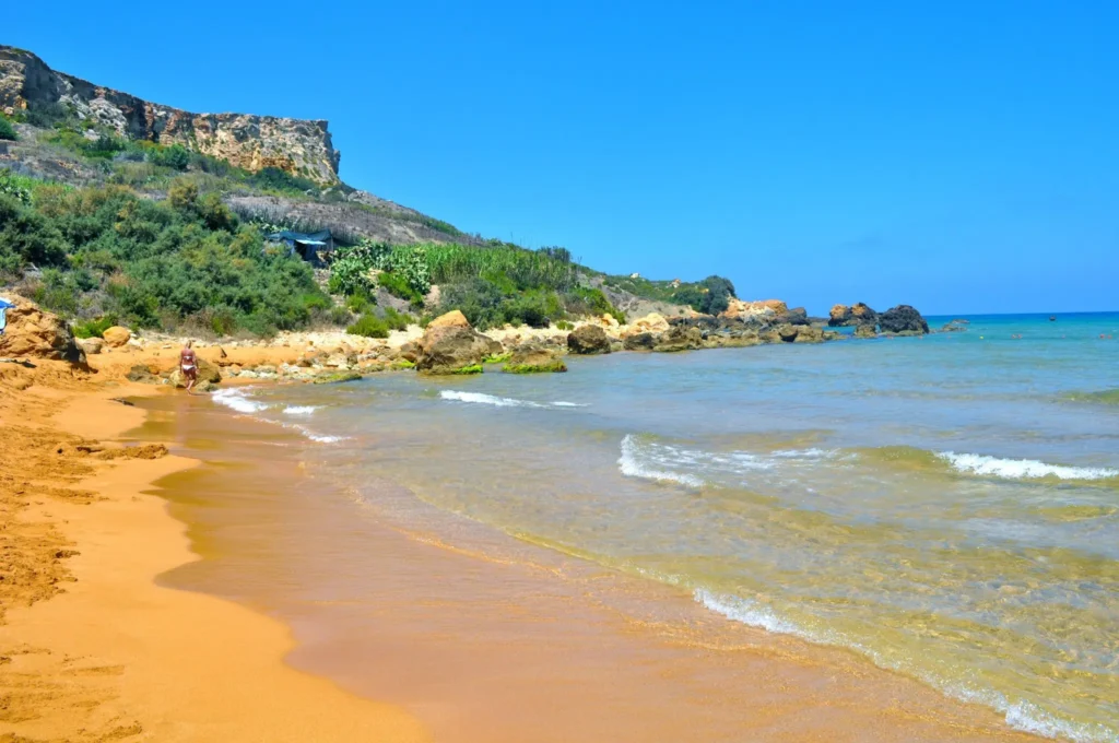 San Blas Beach in Nadur, Gozo, showcasing its golden-red sand, turquoise waters, and lush green surroundings