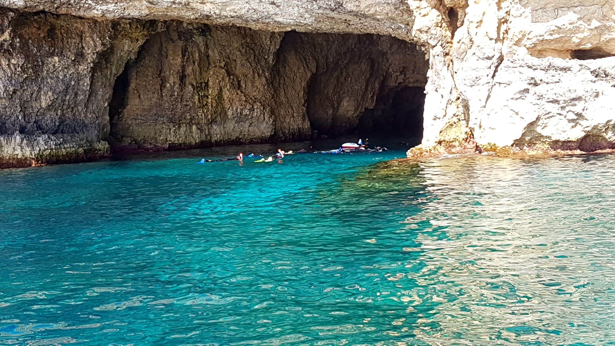 Scenic view of Santa Marija Caves on Comino, Malta, showcasing crystal-clear turquoise waters, rugged limestone cliffs, and hidden sea caves, perfect for snorkeling and boat exploration.
