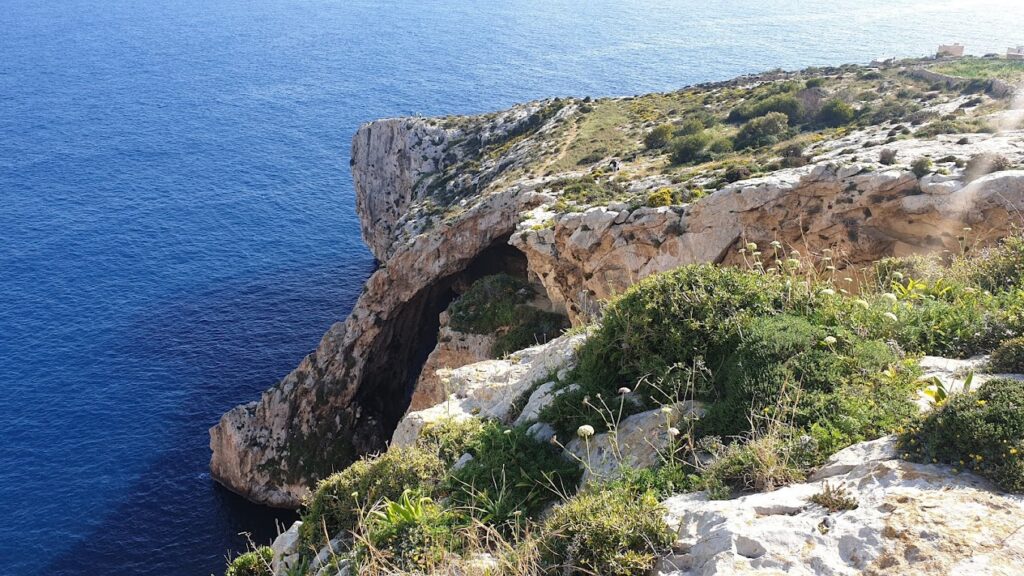 Scenic view of Blue Grotto, Malta, featuring stunning limestone sea caves and crystal-clear turquoise waters under a bright blue sky.