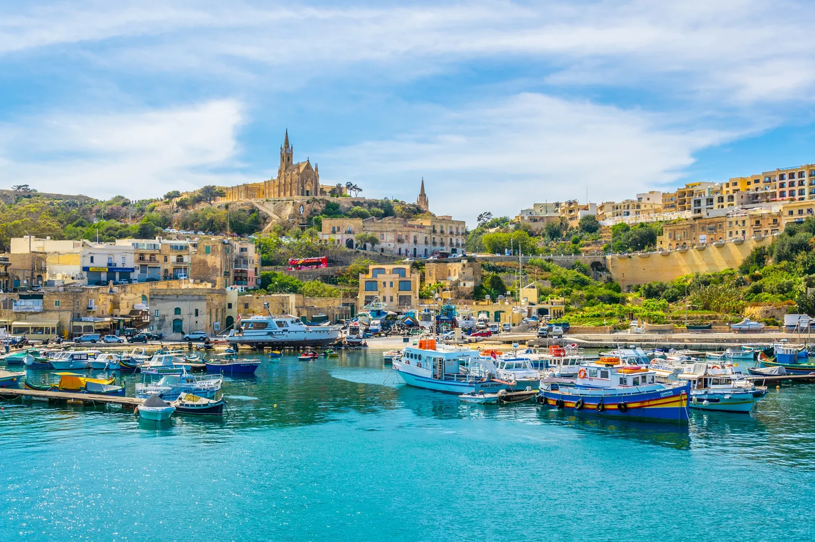 Scenic view of the Island of Gozo, Malta, featuring rugged cliffs, turquoise waters, and historic architecture under a clear blue sky.