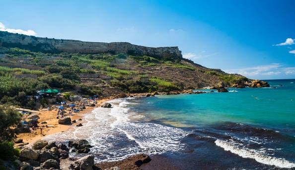 Tranquil San Blas Beach in Gozo, Malta, with soft golden-red sand, clear blue waters, and a peaceful, unspoiled natural landscape.