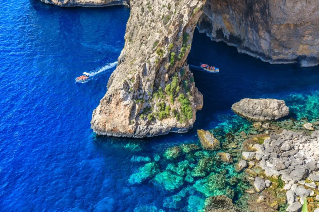 Scenic view of Blue Grotto, Malta, featuring stunning limestone sea caves and crystal-clear turquoise waters under a bright blue sky.