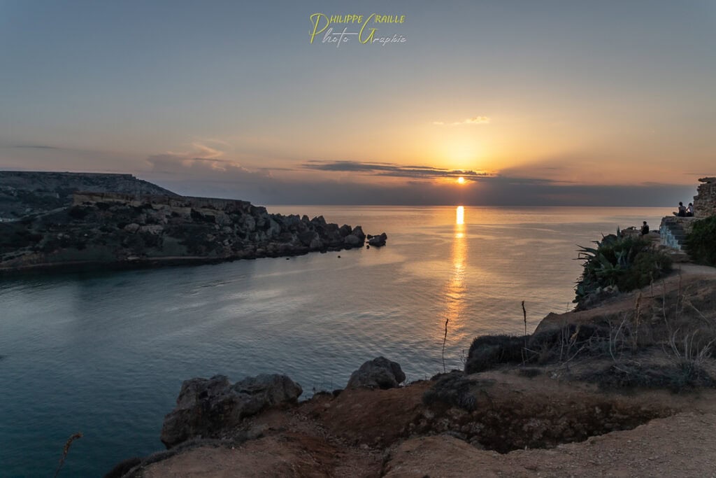Sunset over Għajn Tuffieħa Bay in Malta with golden skies, rugged cliffs, and calm Mediterranean waters