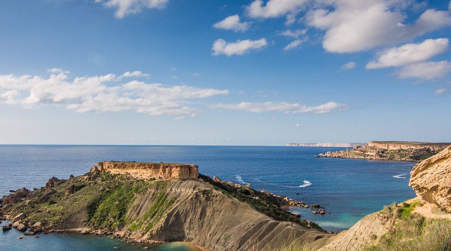 Scenic view of Ġnejna Bay Malta with golden sandy beach, clear blue sea, and limestone cliffs