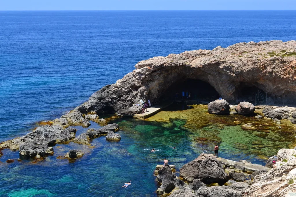 Scenic coastal view of Ghar Lapsi in Malta, featuring crystal-clear turquoise waters, rugged limestone cliffs, and a peaceful natural swimming area.