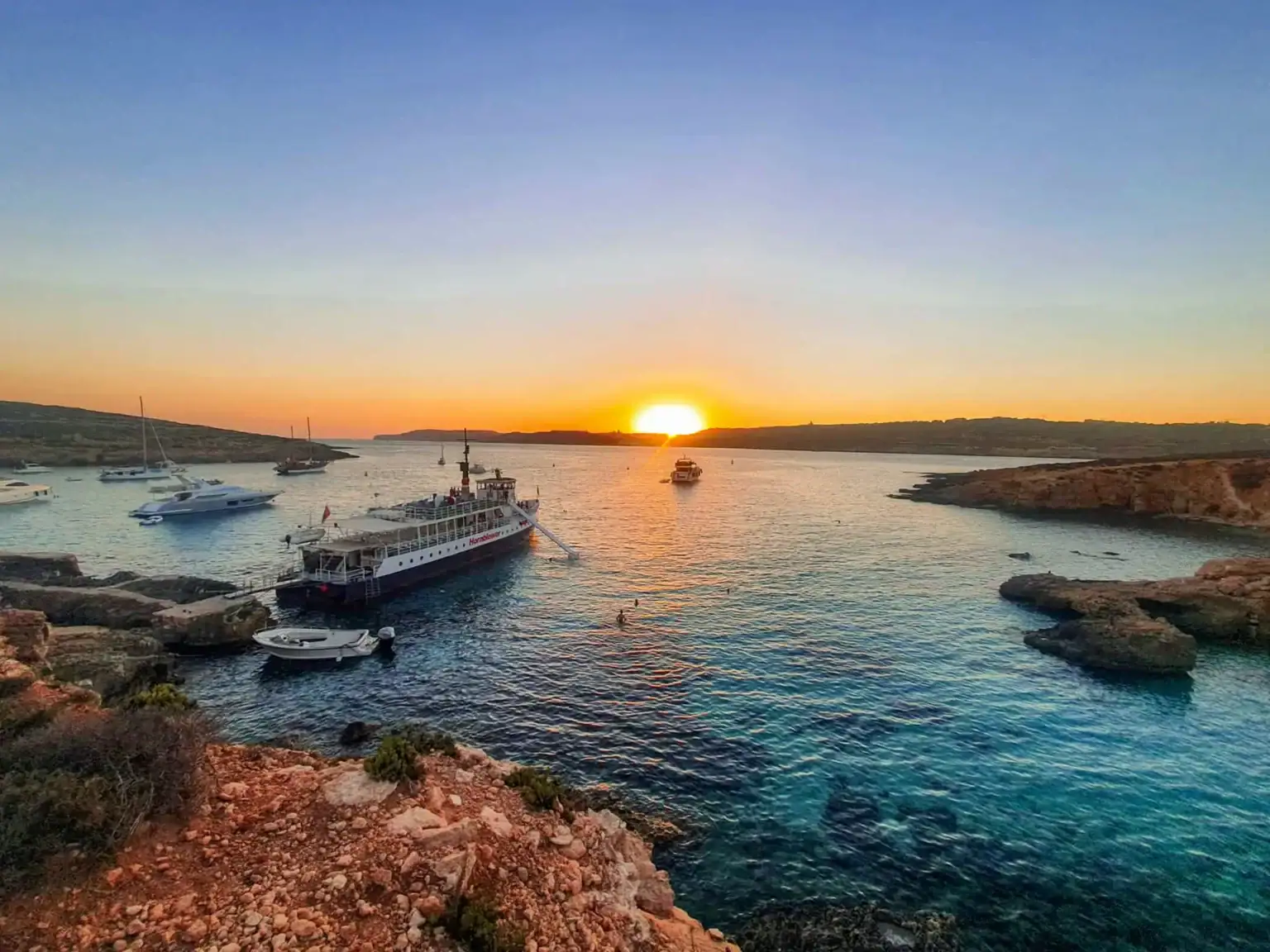 Golden sunset over the Blue Lagoon Malta during a peaceful sunset boat trip, with crystal-clear waters and dramatic coastal cliffs in view.