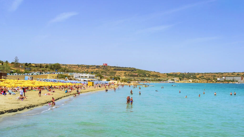 Mellieha Beach Malta with people swimming in the clear blue sea and relaxing on the sandy shore