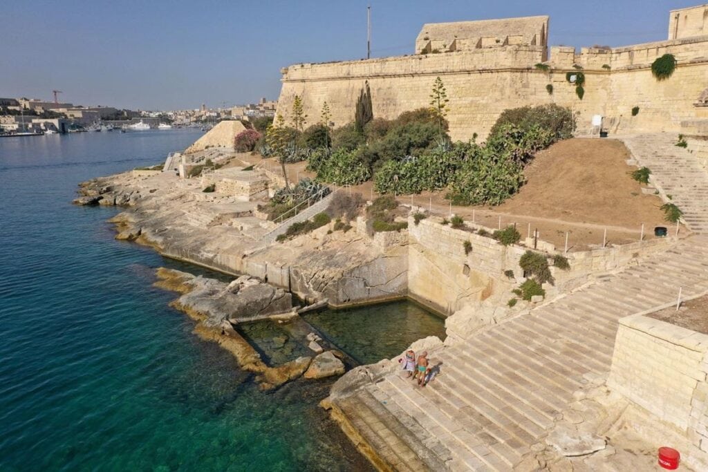 Manoel Island Foreshore with clear blue waters and rocky shoreline, a popular spot for relaxing walks and enjoying beaches near Valletta, Malta.