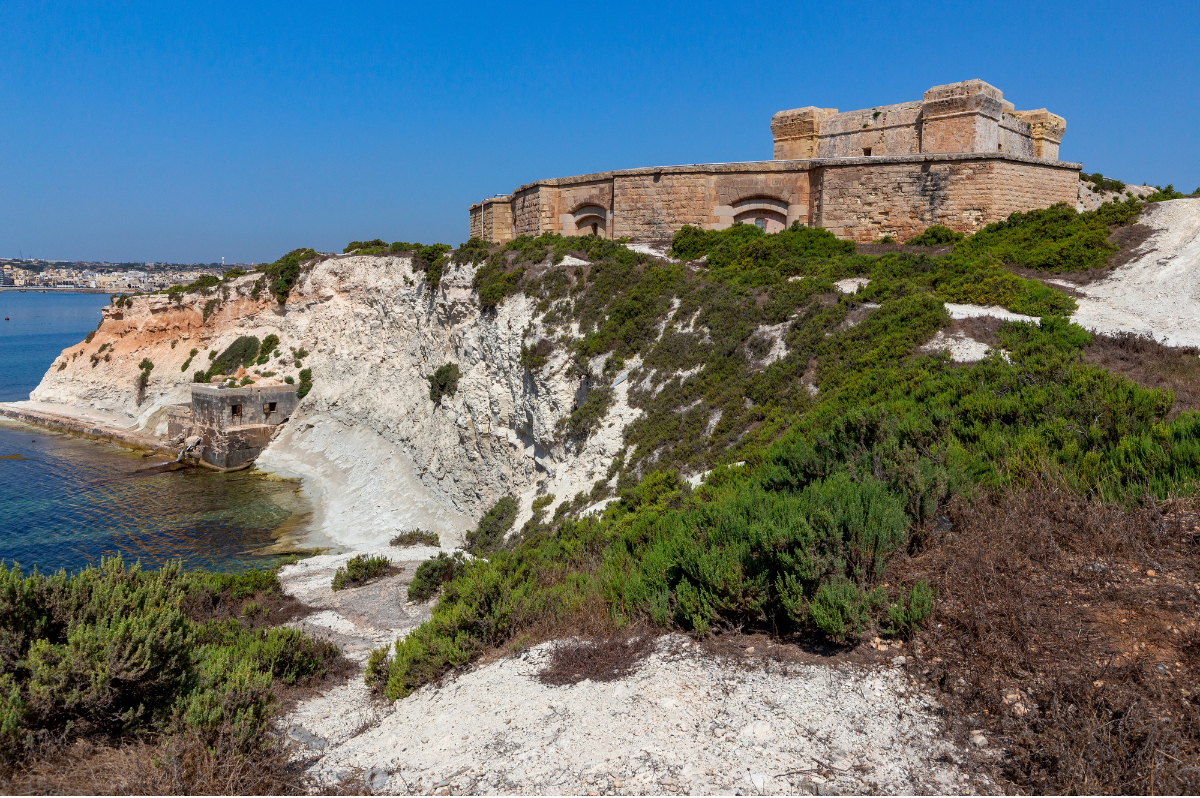 Fort San Lucian (St. Lucian Tower) overlooking the harbor at Marsaxlokk Fishing Village, Malta, with traditional colorful fishing boats in the water.
