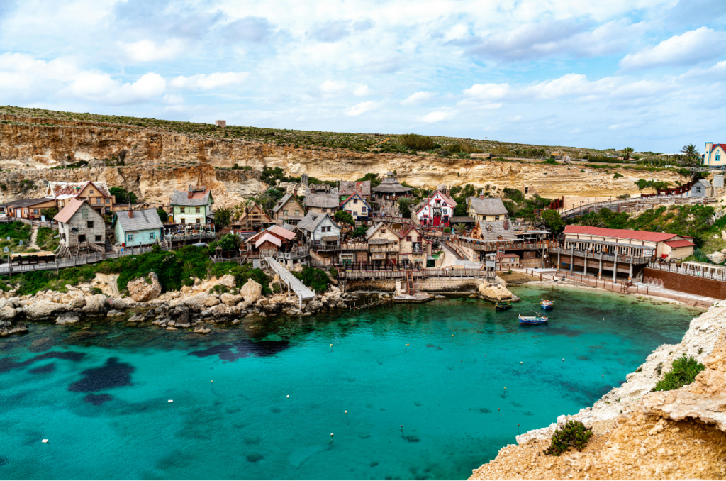 Panoramic view of Popeye Village Viewpoint overlooking the colorful seaside village, cliffs, and turquoise Mediterranean Sea in Malta.