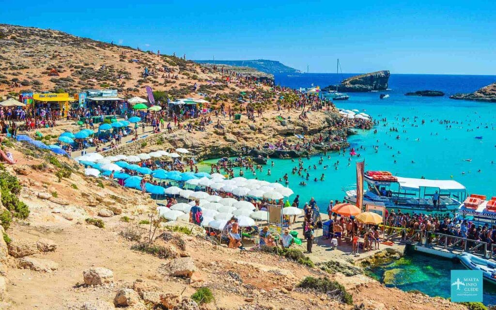 A packed Blue Lagoon in Malta with crystal-clear turquoise water and anchored boats filled with tourists enjoying the popular stop on many cruises from Malta.