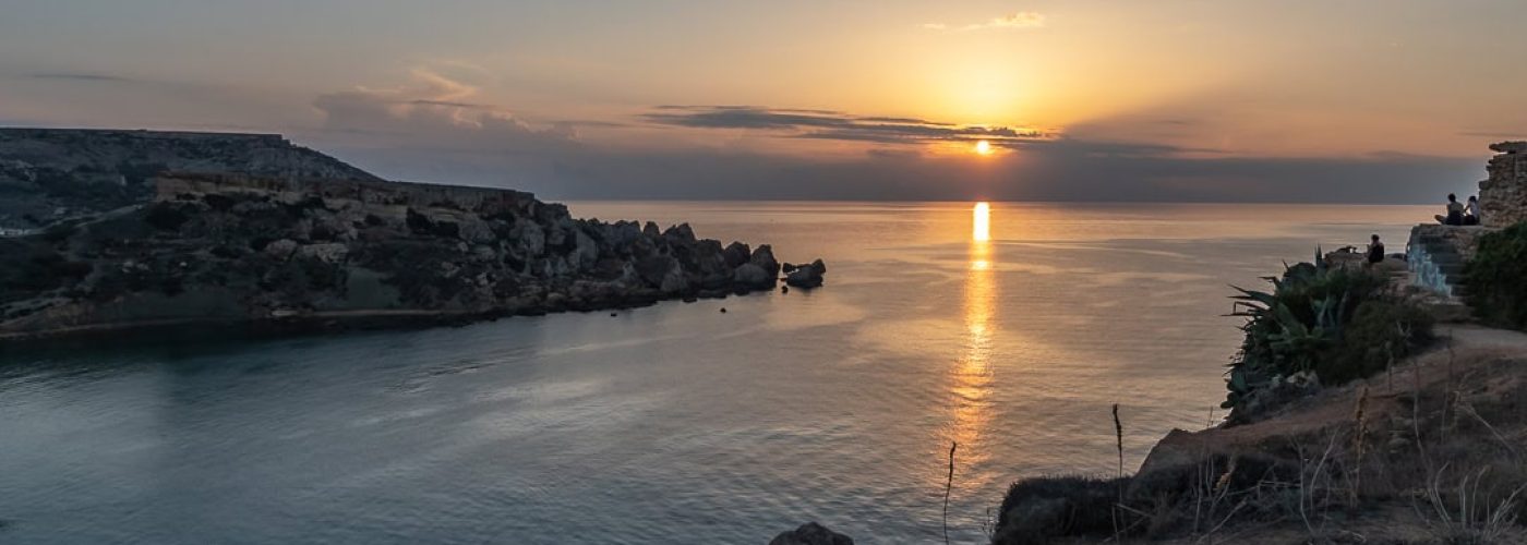 Sunset over Għajn Tuffieħa Bay in Malta with golden skies, rugged cliffs, and calm Mediterranean waters