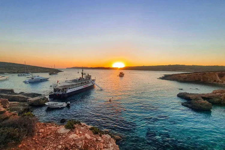 Golden sunset over the Blue Lagoon Malta during a peaceful sunset boat trip, with crystal-clear waters and dramatic coastal cliffs in view. This is one of Malta top spots and ideal for comino sunset cruise tour.