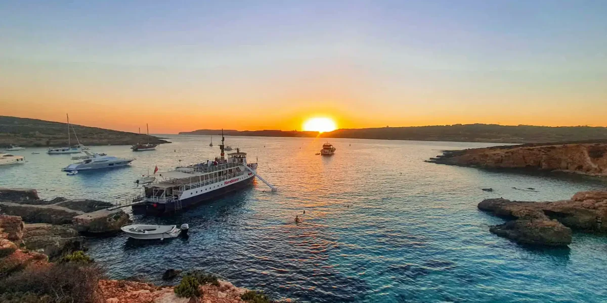 Golden sunset over the Blue Lagoon Malta during a peaceful sunset boat trip, with crystal-clear waters and dramatic coastal cliffs in view. This is one of Malta top spots