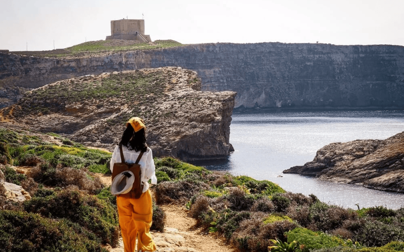 Comino-Hiking Scenic view of a hiker trekking along the rugged cliffs of Comino, Malta, with breathtaking turquoise waters and limestone landscapes in the background.