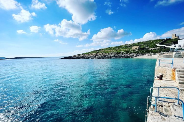 Scenic view of Bamberin Beach with clear blue waters and rocky shoreline, showcasing one of the best beaches in Malta and Gozo for swimming and relaxation.