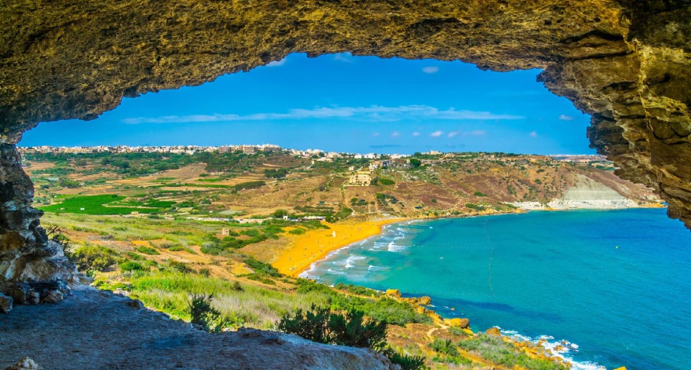 Scenic view of San Blas Beach in Malta, featuring golden-red sand, turquoise waters, and lush green cliffs