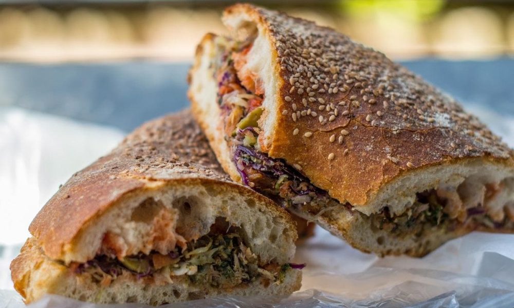 traditional Maltese snack, Ftira Close-up photo of a traditional Maltese snack, Ftira, a round flatbread filled with fresh ingredients such as tomatoes, olives, capers, onions, and tuna, drizzled with olive oil and served on a rustic wooden plate.