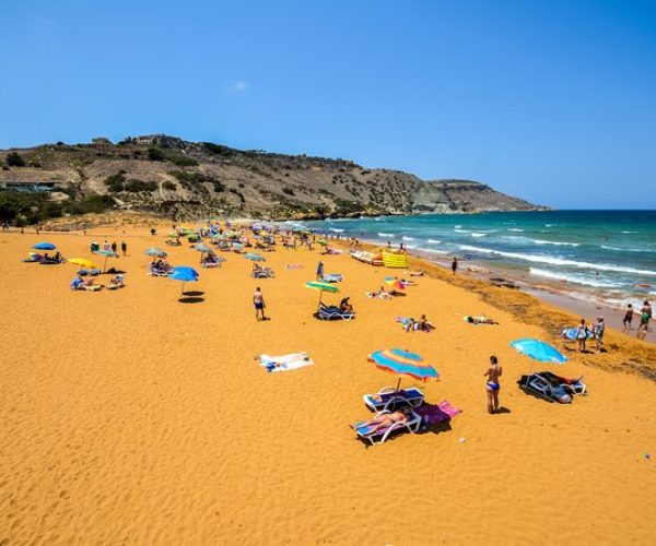 Ramla beach Malta Ramla beach Malta on a bright day, with tourists sunbathing under umbrellas and enjoying the scenic coastline.