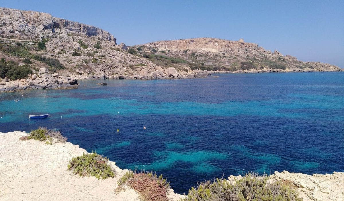 Scenic view of Daħlet Qorrot Beach in Gozo, featuring crystal-clear waters, rugged limestone cliffs, and colourful fishing boats along the shore.